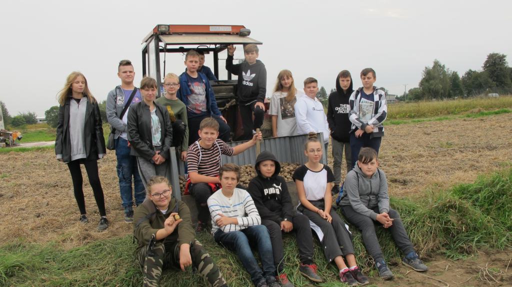 Grupa uczniów stojąca przy traktorze na polu 